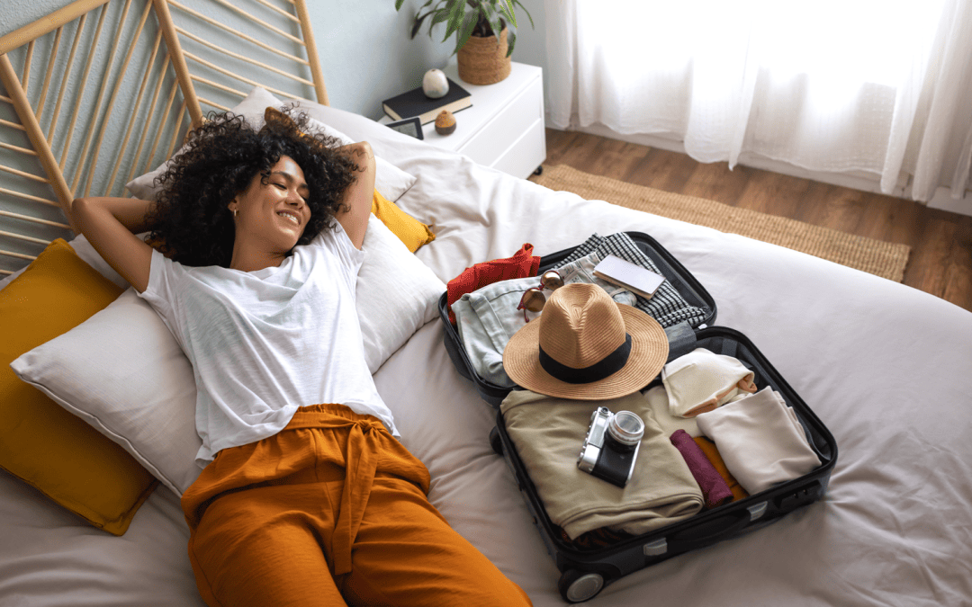 Femme heureuse couchée sur son lit à côté de sa valise ouverte