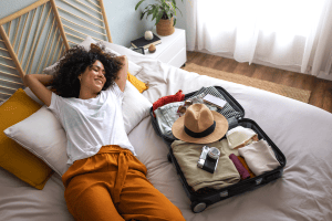 Femme heureuse couchée sur son lit à côté de sa valise ouverte