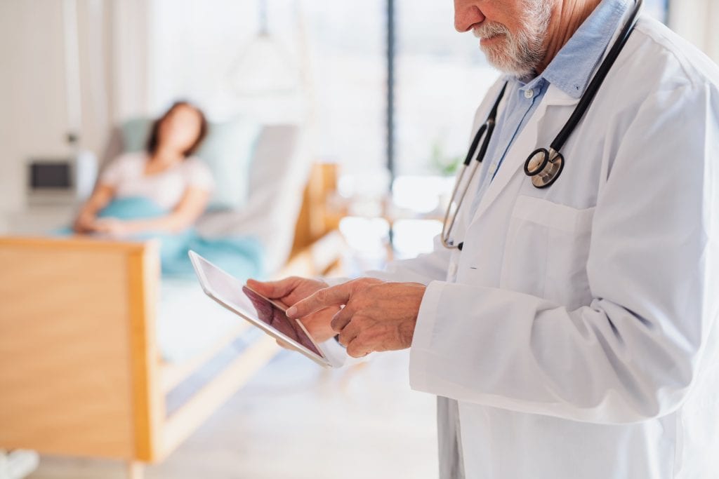 Médecin regardant tablette et patiente en arrière-plan allongée dans un lit d'hôpital