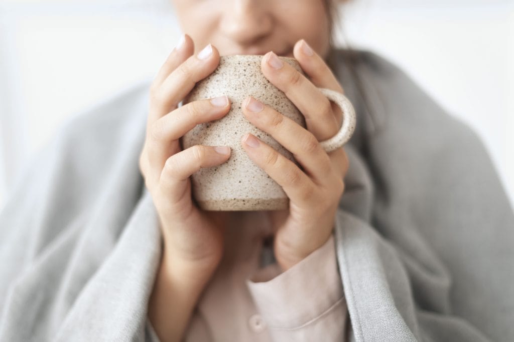 Femme sous un plaid gris tenant une tasse.